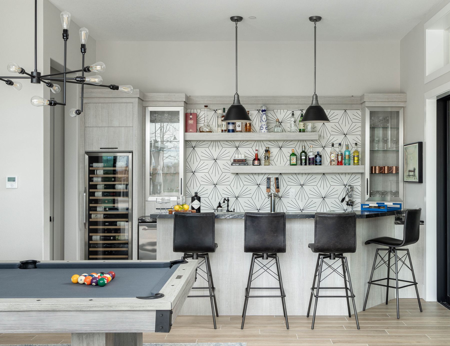A games lounge with a billiard table, bar seating in aged black leather and a graphic starburst tile backsplash.